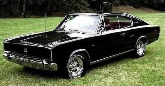A classic black car, possibly a Dodge Charger, is parked on a green grassy field.