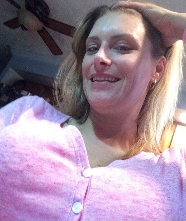 A woman posing for a selfie indoors, wearing a pink cardigan.