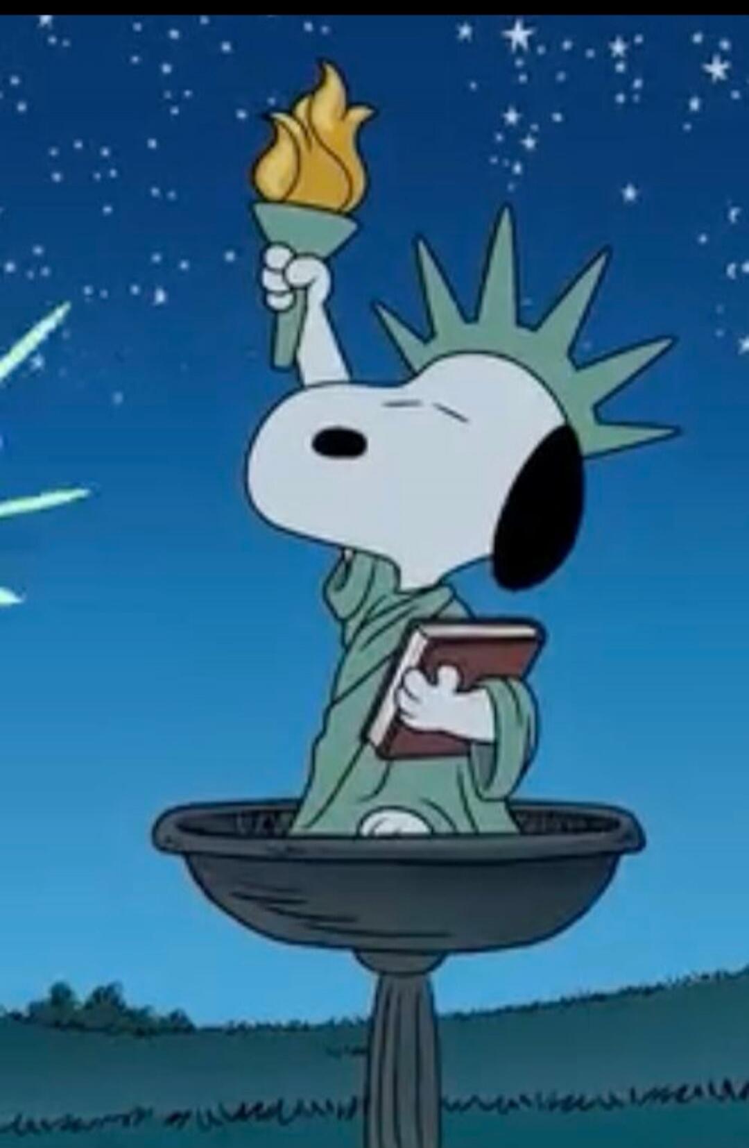 Snoopy dressed as the Statue of Liberty holding a torch and a book.