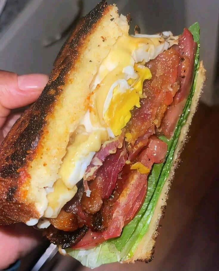 Photo of a bacon, egg, and cheese sandwich with lettuce on toasted bread.