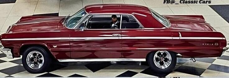 A classic red car, possibly a Chevrolet Impala, is parked on a black and white checkered floor. A person is visible inside the car. The text 'FB@_Classic Cars' is visible in the top right corner.