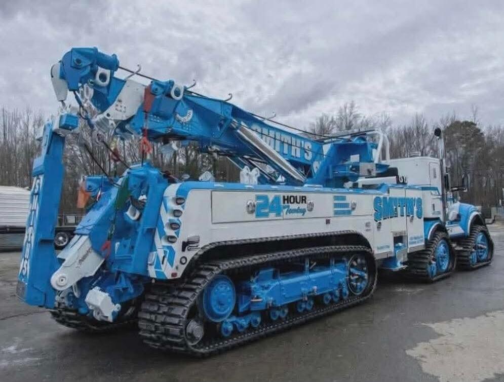 Blue heavy-duty tracked crane vehicle with a long articulated arm. Visible text on the side includes '24 HOUR' and other branding markings.