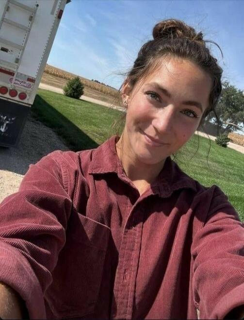 A young woman taking a selfie outdoors, wearing a maroon shirt, smiling.