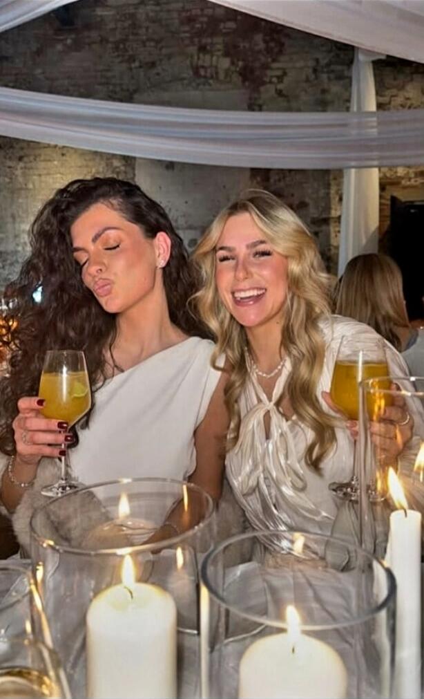 Two women at a candlelit dinner toasting with orange drinks.