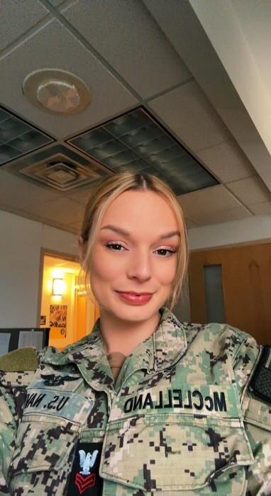 A young woman in a US Navy uniform, smiling at the camera. The name 'MCCLELLAND' is visible on her uniform.