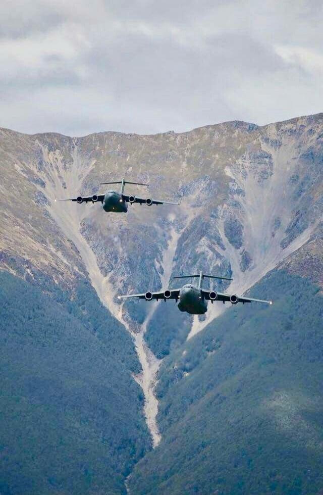 Two military transport planes flying through a mountain pass.