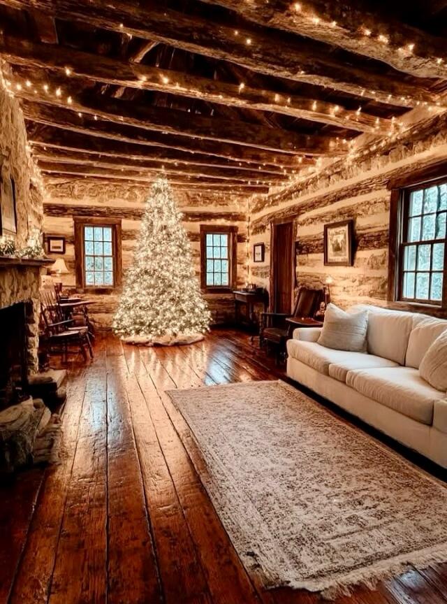 A cozy log cabin living room with a lit Christmas tree, string lights, wooden floors, a white sofa, rug, and rustic decor.