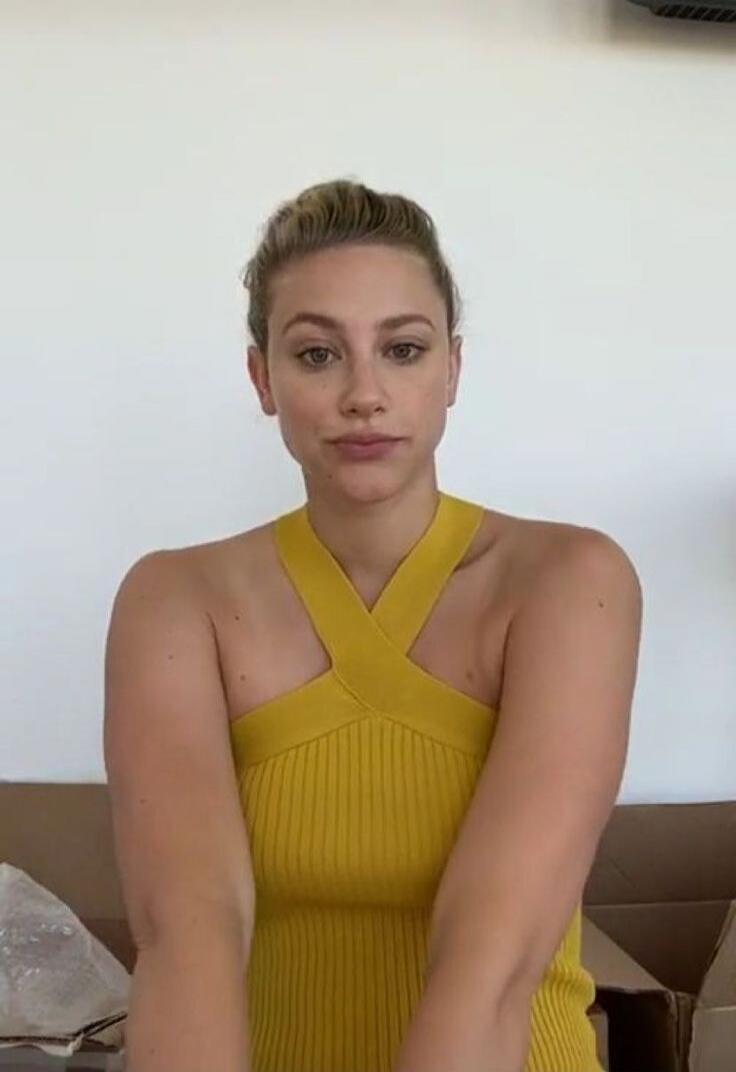 A woman posing indoors wearing a yellow cross-strap sleeveless top.