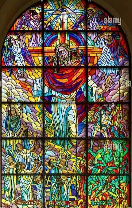 Stained glass window depicting various religious scenes. The central panel features Jesus Christ. Above, an Eye of Providence is visible. Other panels show angels, people praying, and scenes of judgment or suffering. Text at the bottom reads 'STAD PRZYJDZIE SADZIC'.