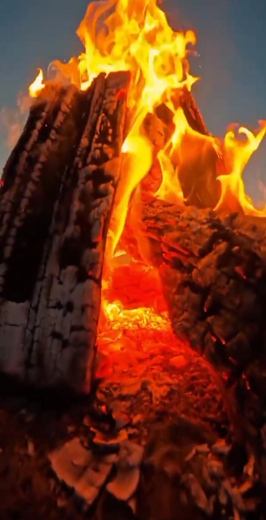 Bonfire with large flames rising from stacked logs.