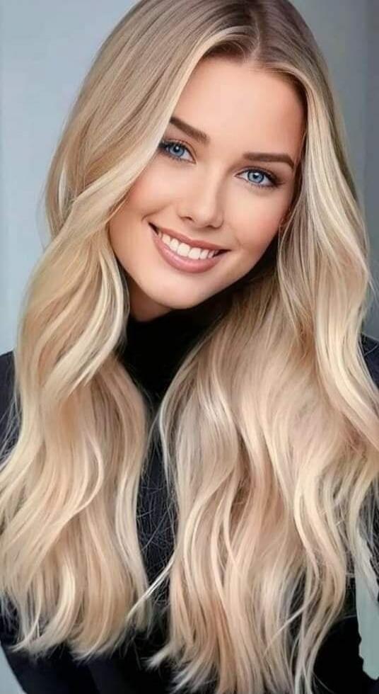 A smiling woman with long wavy blonde hair wearing a dark top.