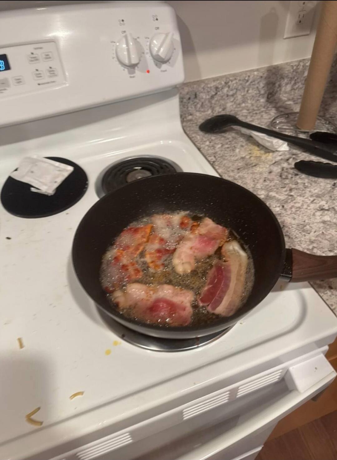 Bacon frying in a pan on an electric stove.