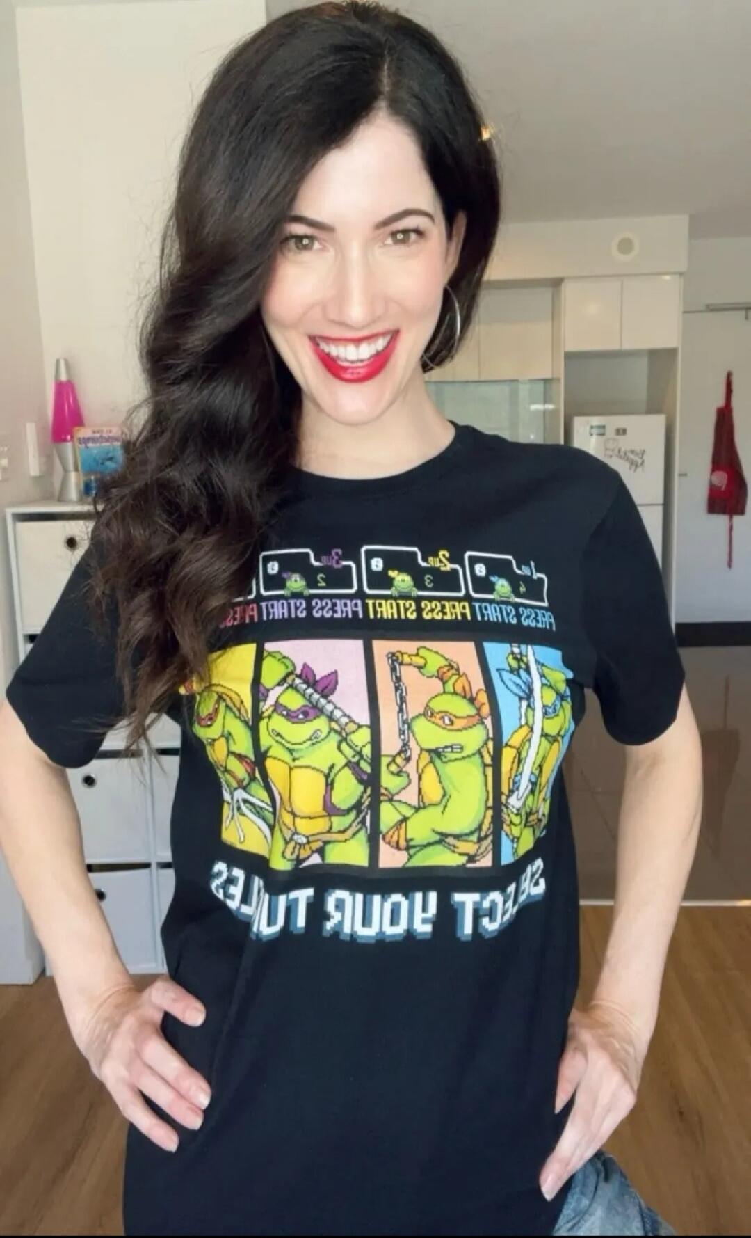 A woman wearing a black T-shirt featuring a Teenage Mutant Ninja Turtles graphic with four turtles and colored panels.