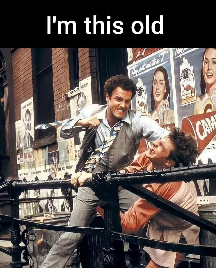 I'm this old. A still from the movie 'Once Upon a Time in America' showing two men, one smiling menacingly while holding the other by the collar during a struggle on a bridge, with vintage posters in the background.