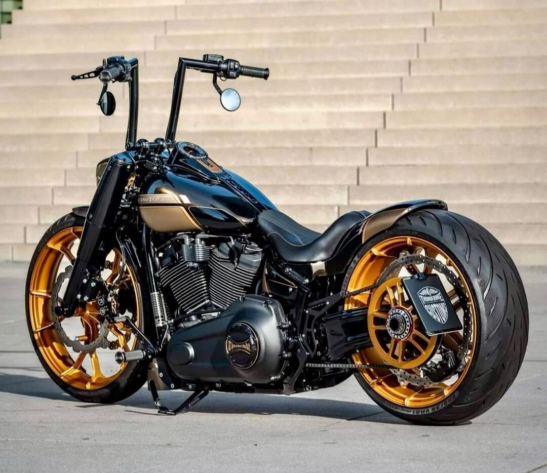 A custom black and gold motorcycle with large handlebars and golden wheels, parked outdoors.