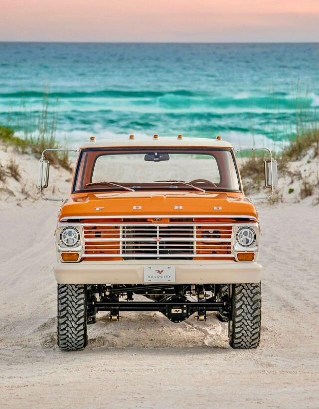 An orange Ford truck on a sandy beach with the ocean in the background.