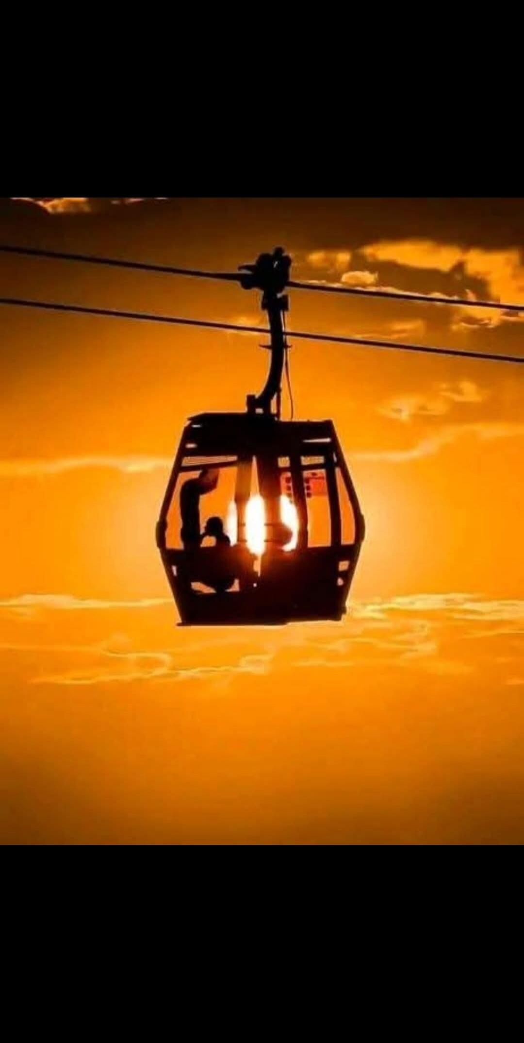 The sun is setting behind a cable car, casting a warm orange glow over the clouds.
