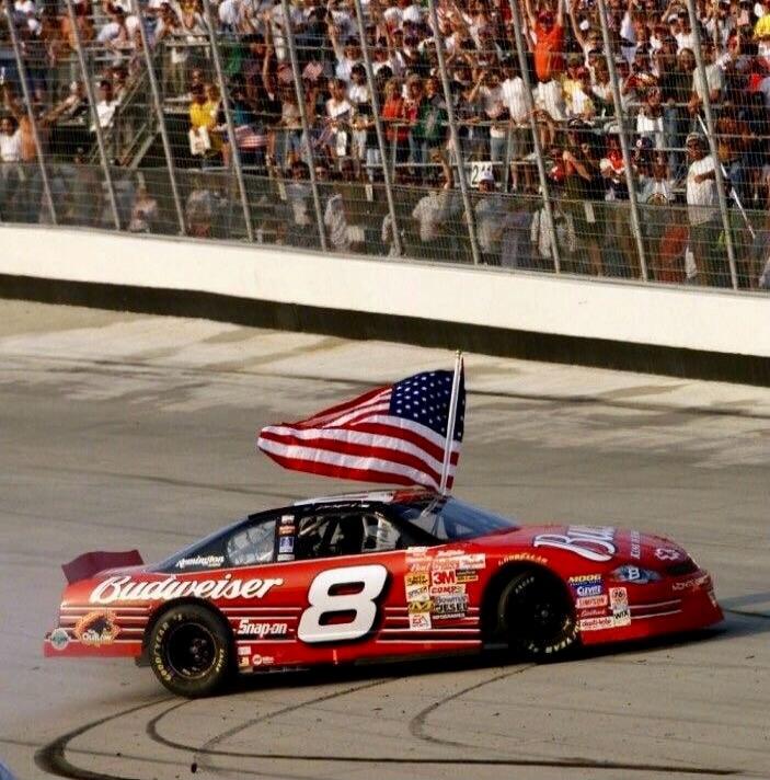 Budweiser Snap-on 8 3M Goodyear MOOG Gatorade BOSCH WIX COMP Given Raybestos ACDelco Edelbrock Holley MSD Simpson K&N Mobil 1 Champion ARP Clevite Fel-Pro Mr. Gasket Permatex Earl's Moroso Taylor. A red race car with the number 8 on its side, adorned with an American flag, is on a race track. A cheering crowd is visible in the background.