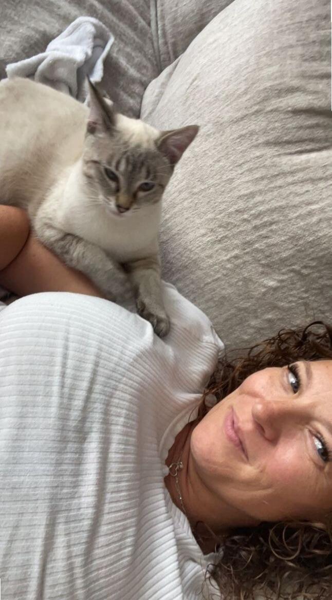 A woman lying on a couch with a cat resting on her chest.