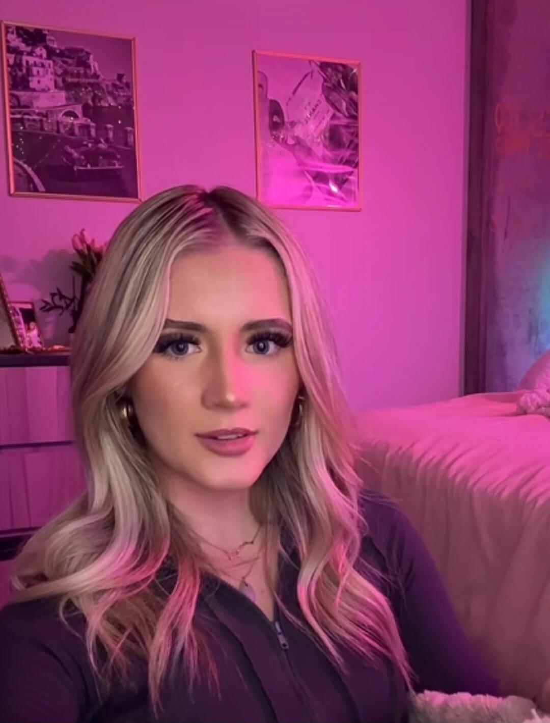 A woman with blonde hair in a pink-lit room.