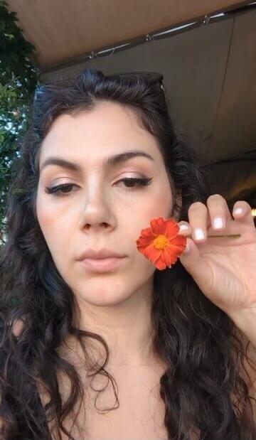A woman outdoors holding a red flower near her face.