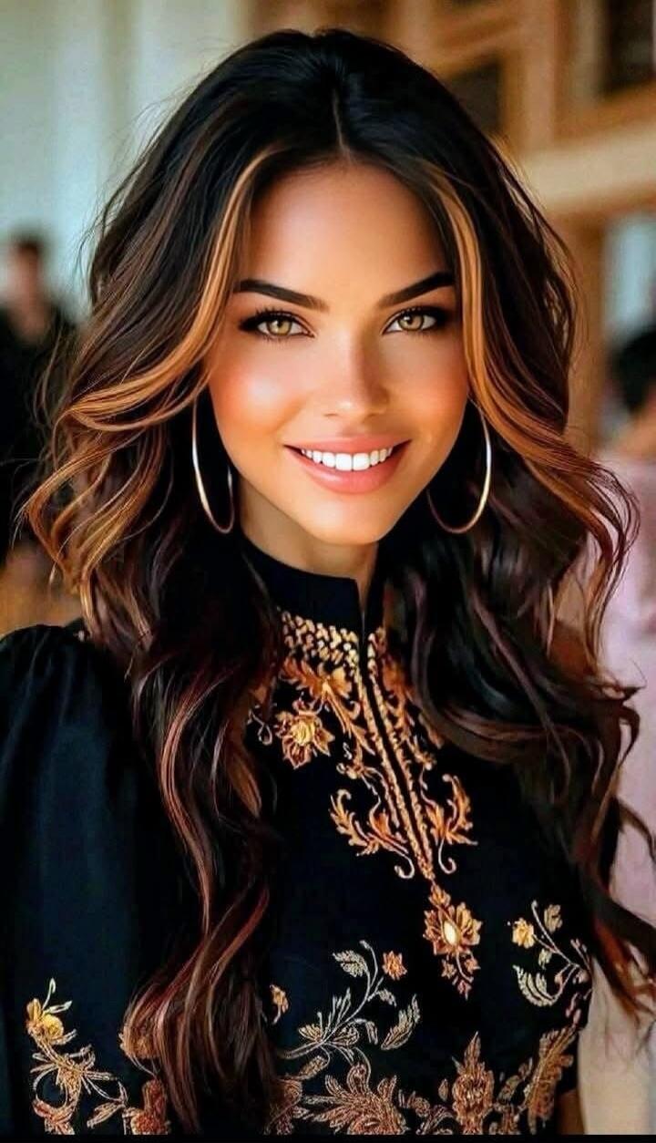 A smiling woman with long wavy hair, large hoop earrings, and a black embroidered top.