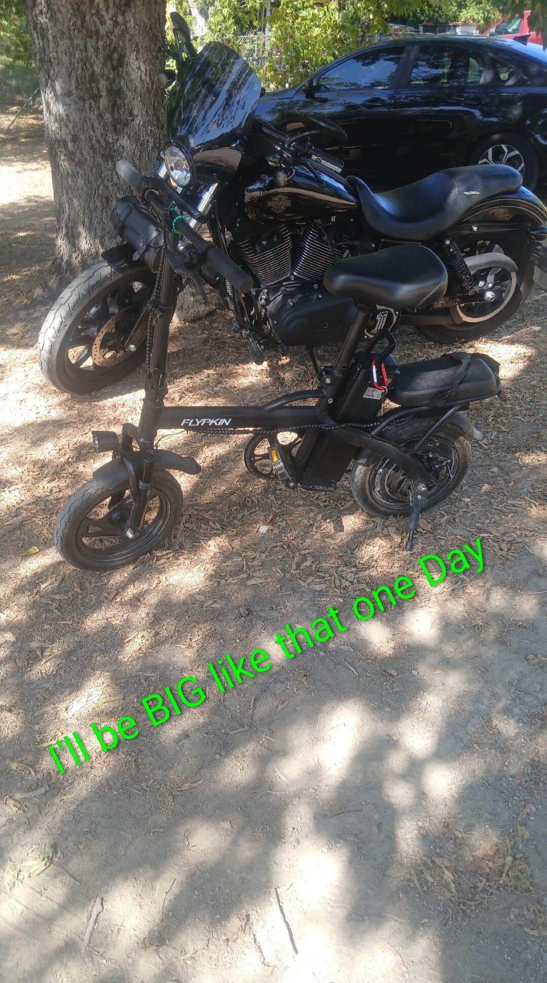 I'll be BIG like that one Day. A small electric bike is parked in front of a large black motorcycle.