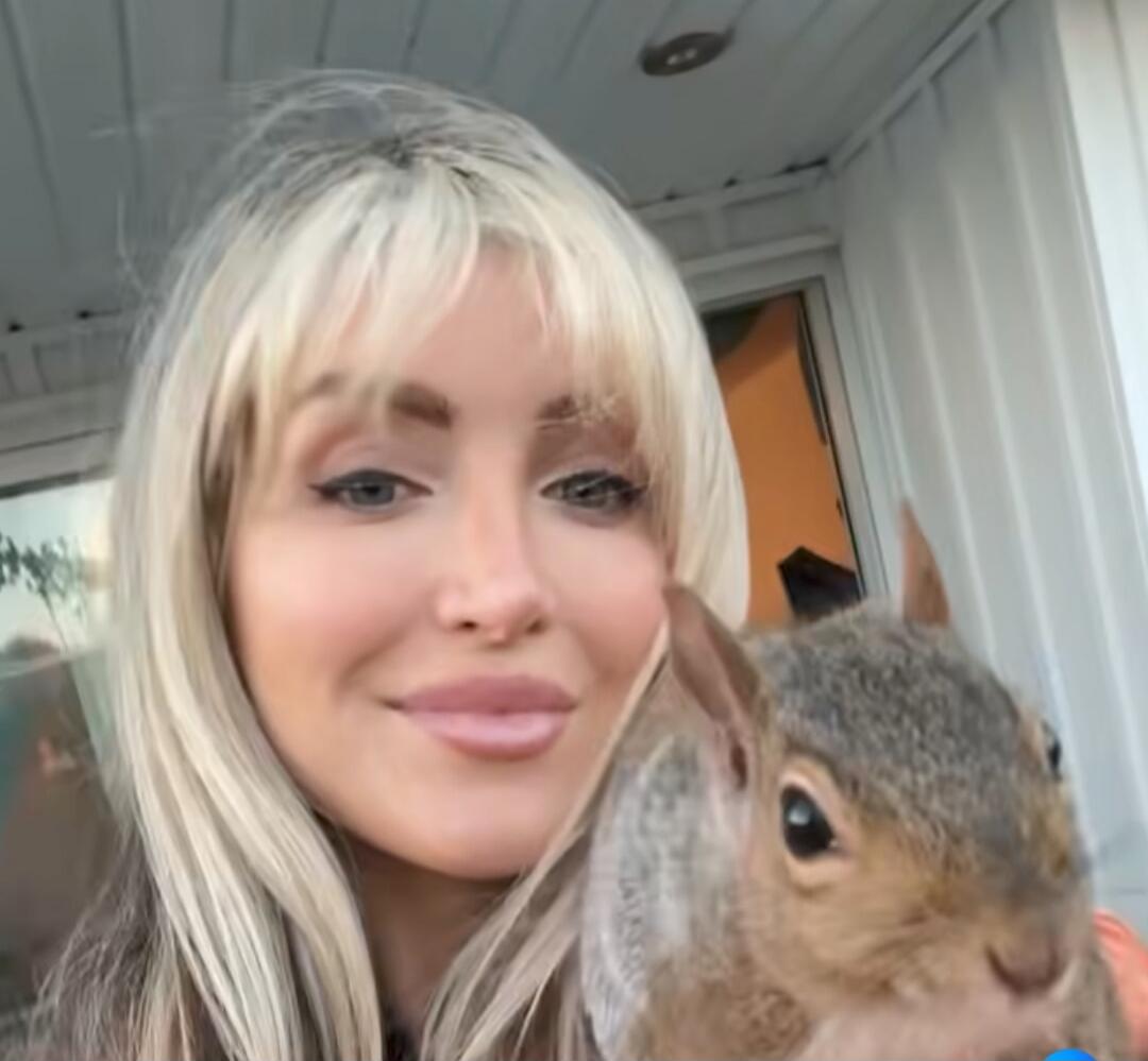 A woman with blonde hair smiling while holding a rabbit.
