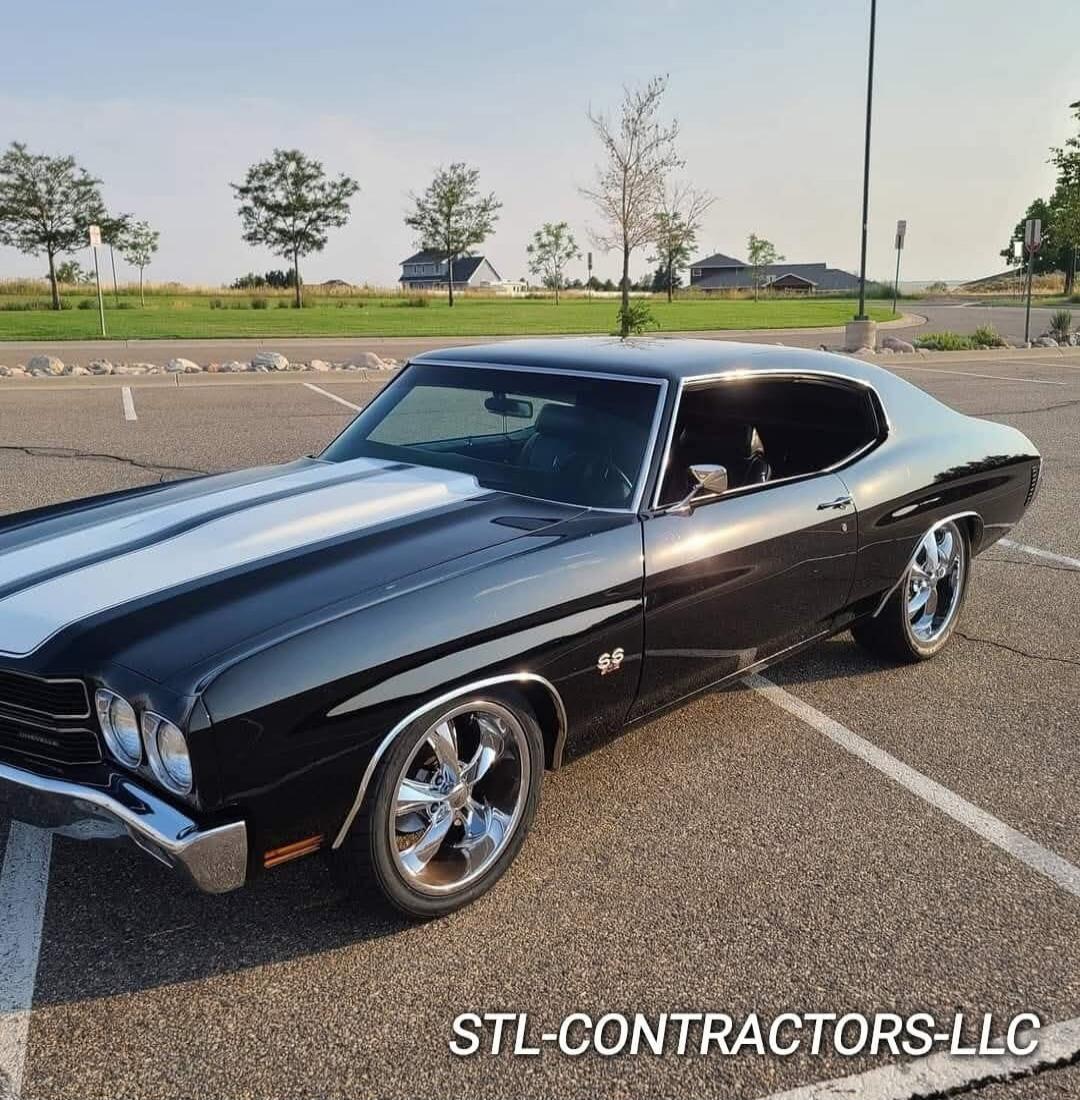 A classic black Chevrolet Chevelle SS with white racing stripes on the hood, parked in a parking lot. Text on image: STL-CONTRACTORS-LLC.