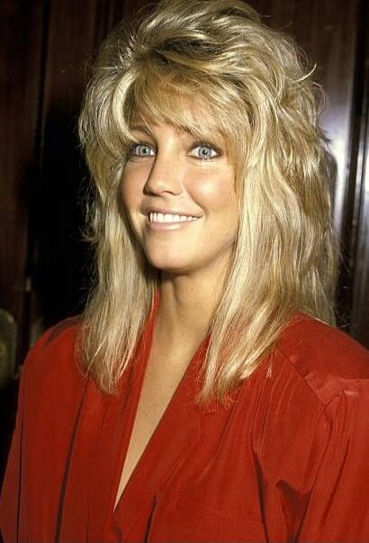 Portrait of a smiling woman with voluminous blonde hair wearing a red outfit.