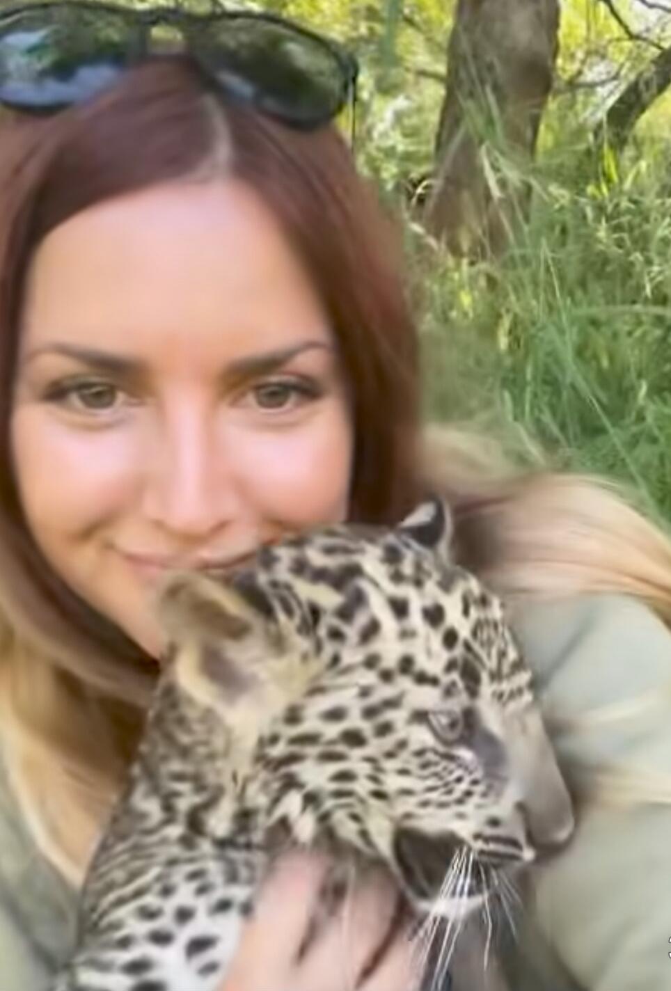 A woman holding a leopard cub outdoors.