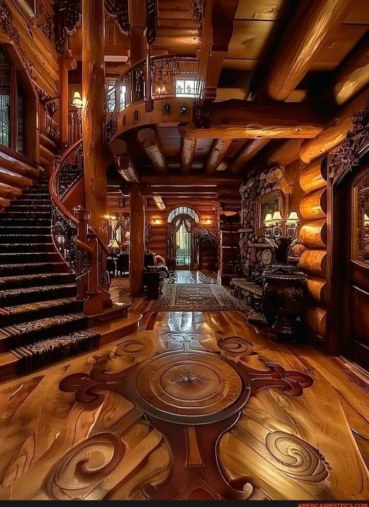 Luxurious log cabin foyer with rich wood paneling, a curved stairway, carved floor inlays, and warm ambient lighting.