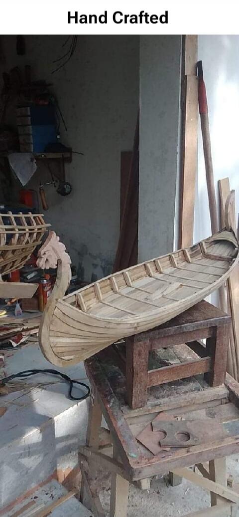 Hand Crafted. A detailed wooden model of a boat, possibly a Viking longship, is displayed in a workshop. The boat shows intricate craftsmanship with its wooden planks and a carved figurehead.