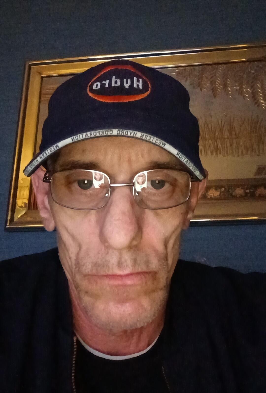 A man wearing a dark blue baseball cap with 'HydrO' (reversed) on the front and 'WESTERN HYDRO CORPORATION' (reversed) on the brim. He is also wearing glasses and looking directly at the camera.
