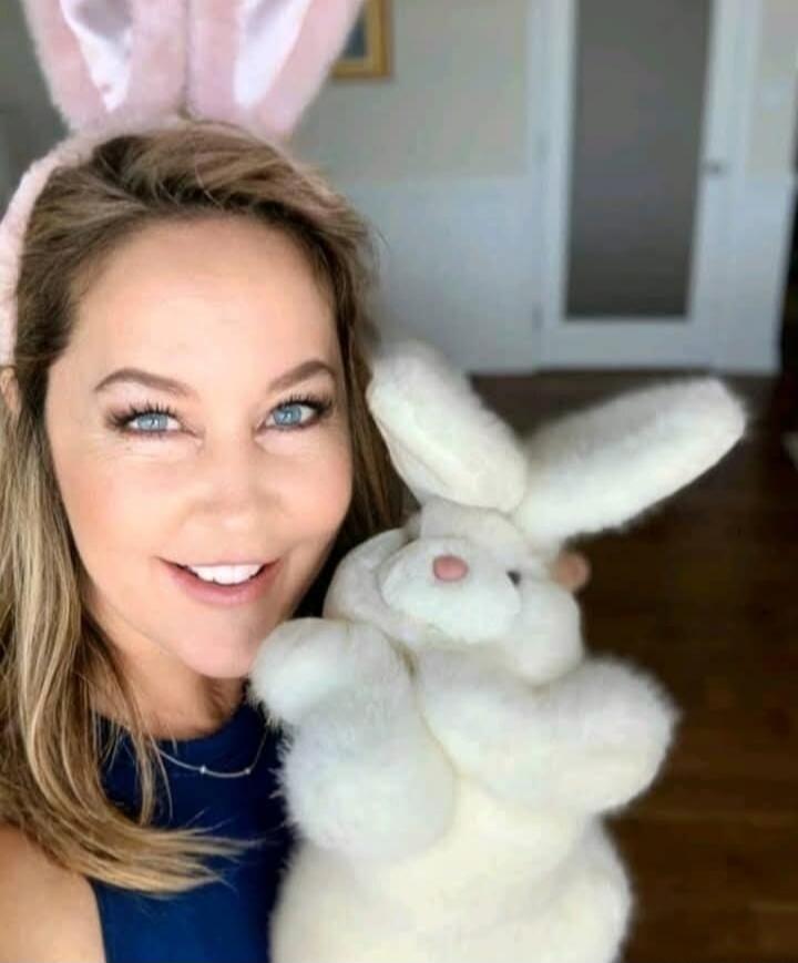 A woman with pink bunny ears smiles while holding a fluffy white stuffed bunny.