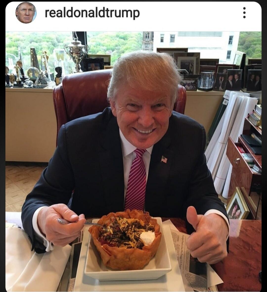 realdonaldtrump. Donald Trump is seen smiling and giving a thumbs-up while eating a taco bowl at a desk. The image is from a social media post by 'realdonaldtrump'.