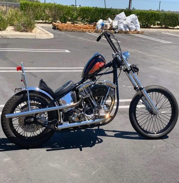 A custom chopper motorcycle with long front fork, black and chrome finish, flames on the fuel tank, parked in a lot.