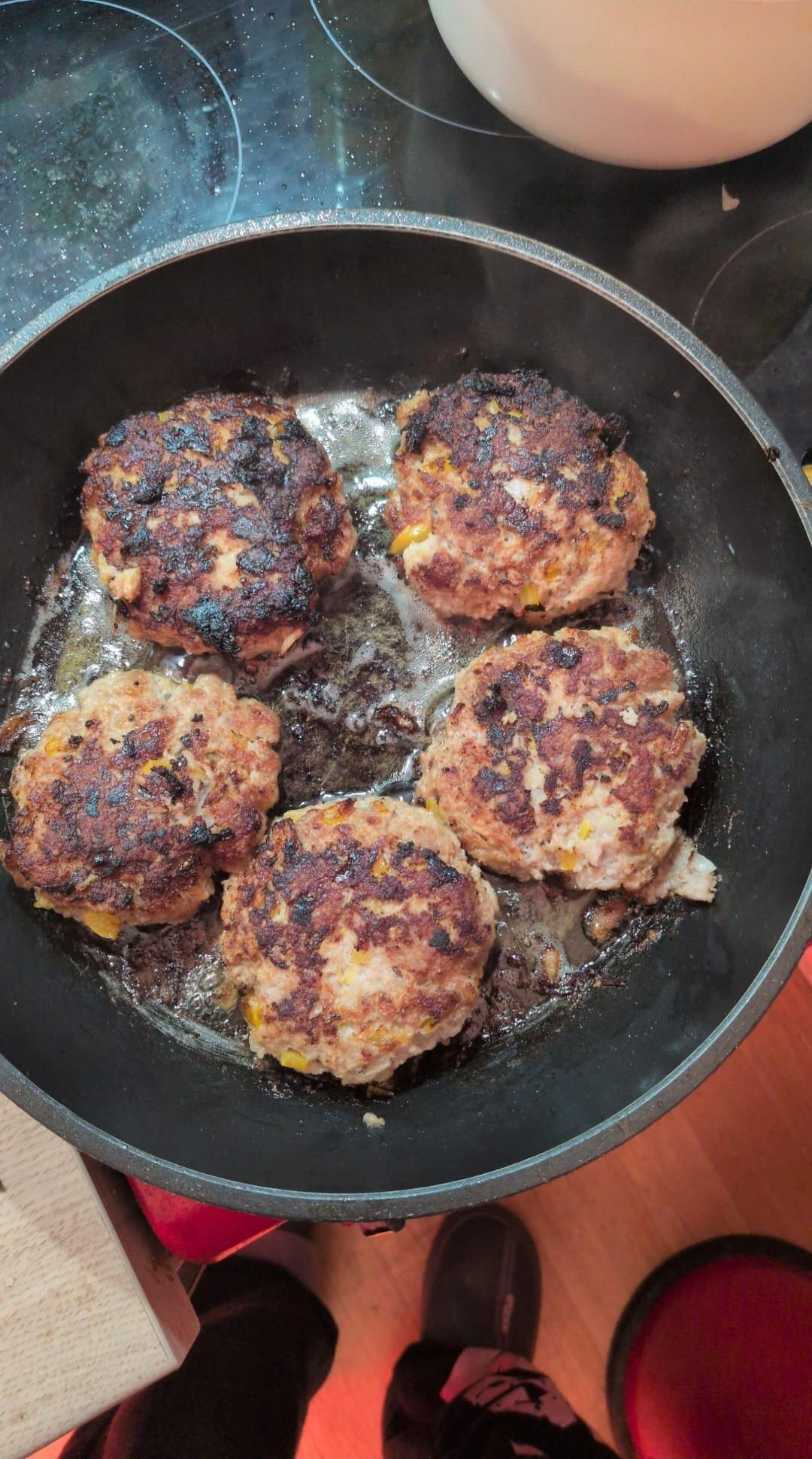 Five burgers are frying in a pan.