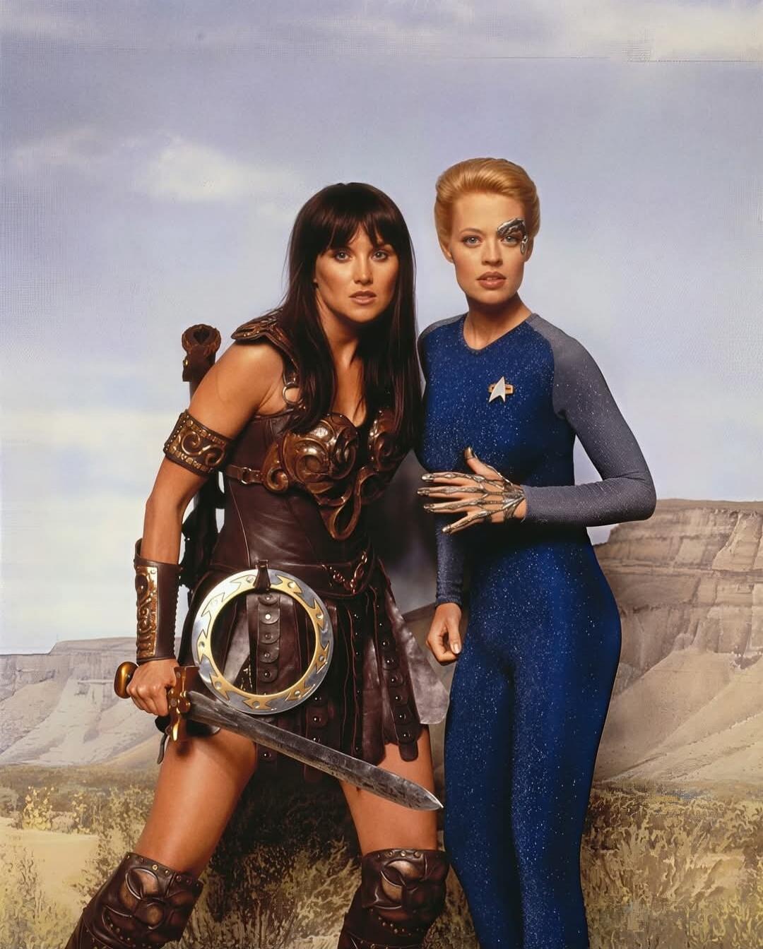 Two women in fantasy armor and jumpsuit stand in a desert landscape.