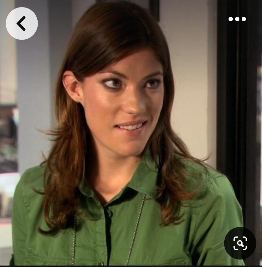 A woman with brown hair wearing a green shirt looking to the side with a skeptical/curious expression.