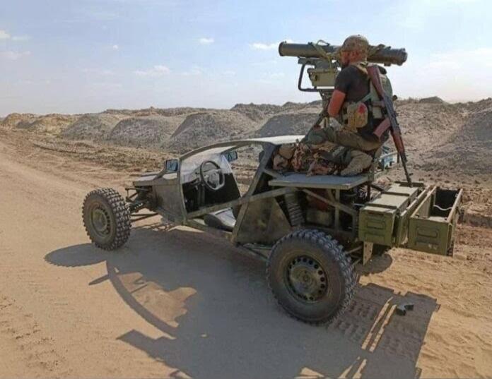 A desert dune buggy with a mounted gun on the back, a person in gear seated on the vehicle.