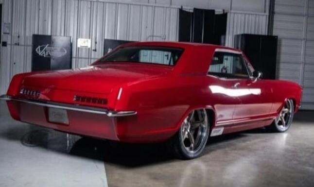 A classic red car is parked in a garage or studio. The car has a sleek design with chrome accents and custom wheels.