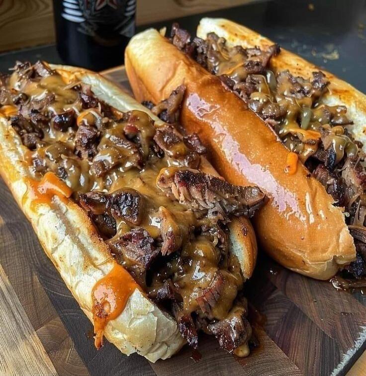 Two delicious cheesesteak sandwiches on a wooden board.