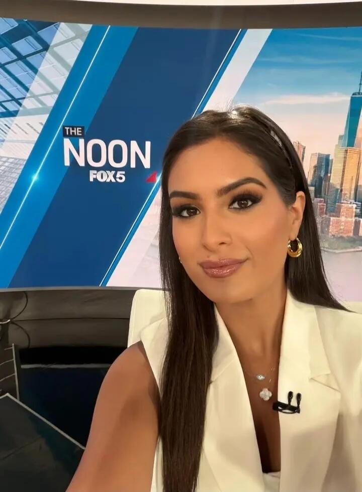The Noon Fox 5. A woman, likely a news anchor, takes a selfie in front of a screen displaying the news program title and a cityscape.