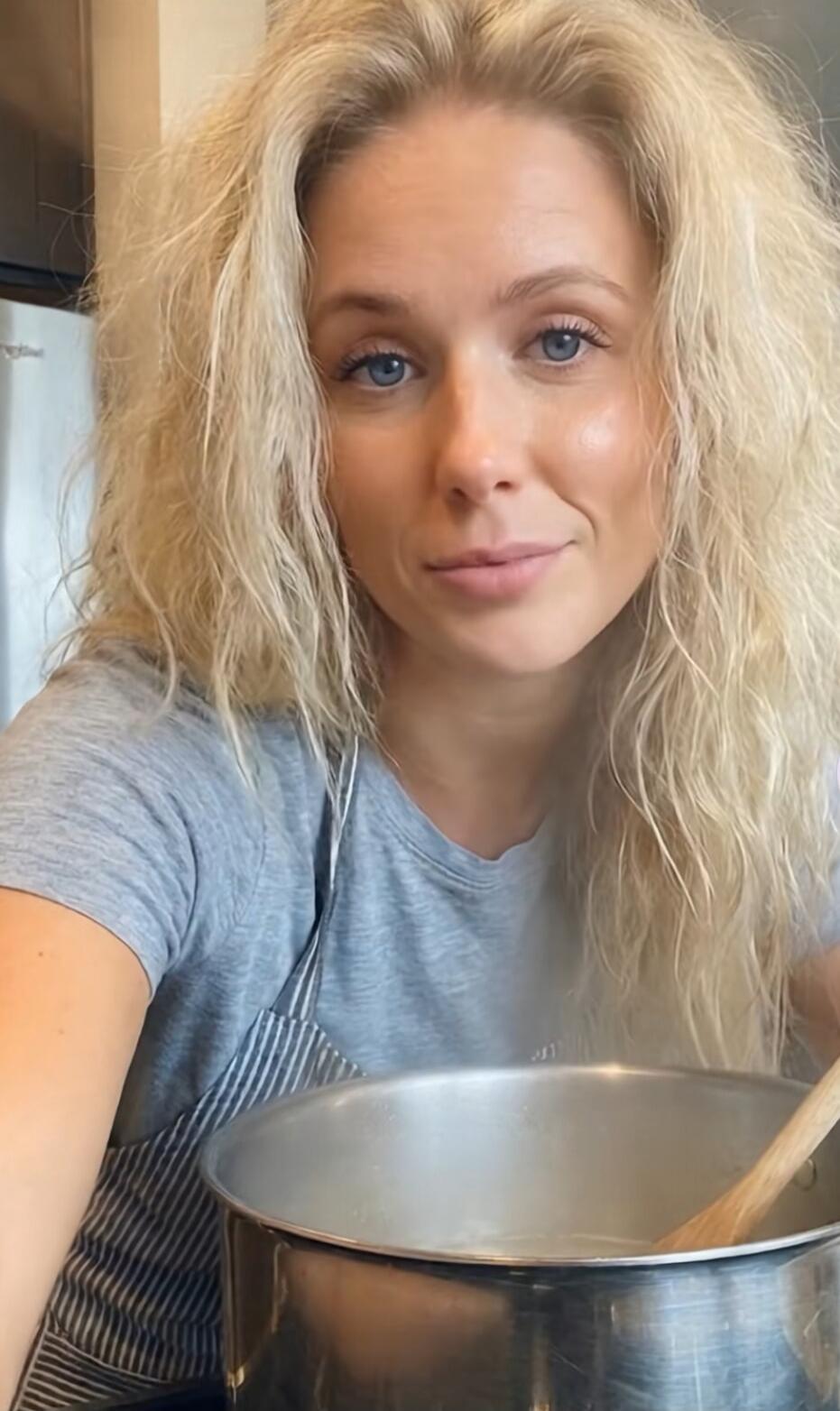 A blonde woman is cooking in a kitchen, stirring a pot.