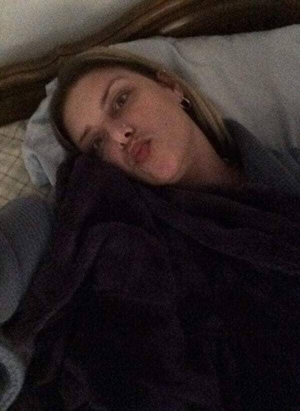 A person lying in bed, under dark blankets, making a pouty face at the camera.