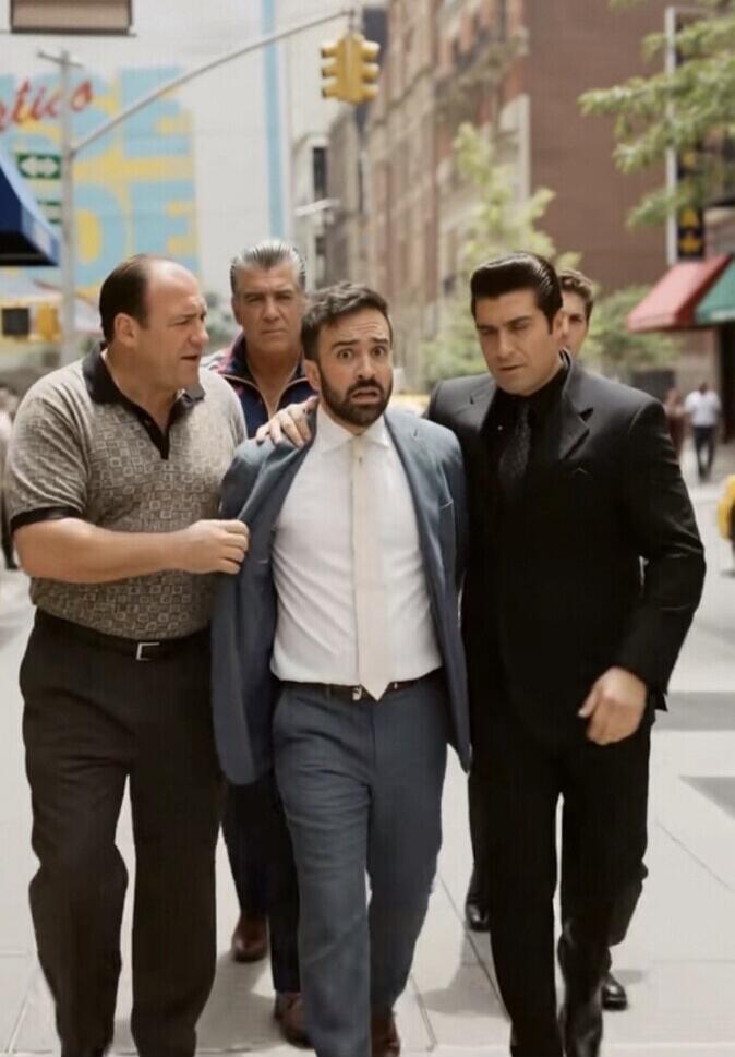 A man in a suit is being escorted by two other men, one resembling Tony Soprano, on a city street. The man in the suit has a surprised or scared expression.