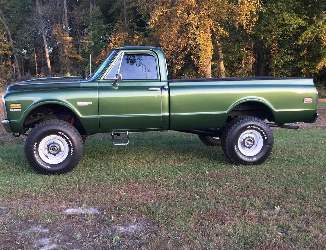 Green vintage pickup truck with lifted suspension in a grassy field.