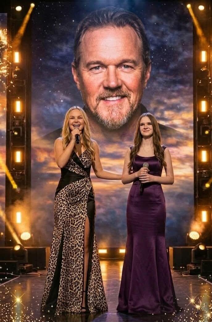 Two young women are singing on stage. Behind them is a large screen with a man's face.