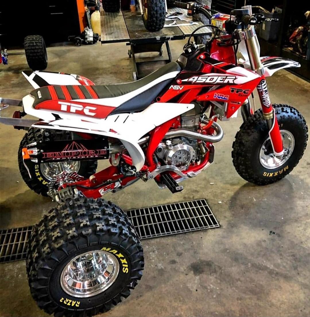Red and white quad/ATV with 450R decals, aggressive off-road tires, in a workshop setting.